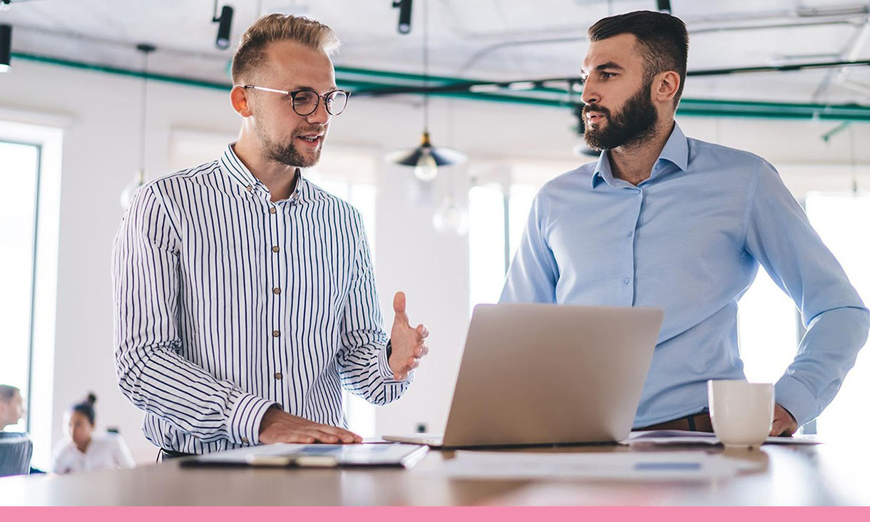 Two coworkers discuss something on a laptop.