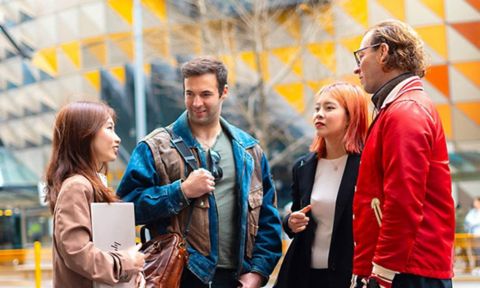 A group of students stand and chat in an outdoor setting