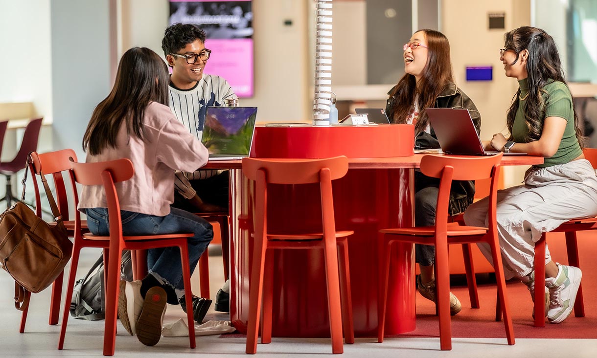 Four international students smiling together and discussing a topic in a classroom