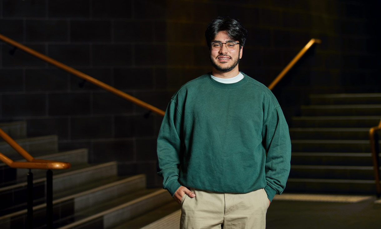 A student in a green jumper standing infront of staircases 